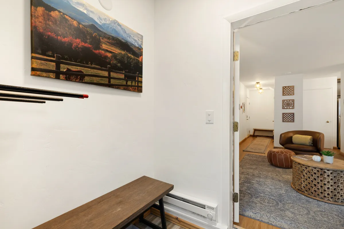 A cozy entryway featuring a wooden bench beneath a striking mountain landscape artwork. The doorway leads into the rest of the home, and the area is spacious enough to serve as a transition zone for removing shoes and storing gear.