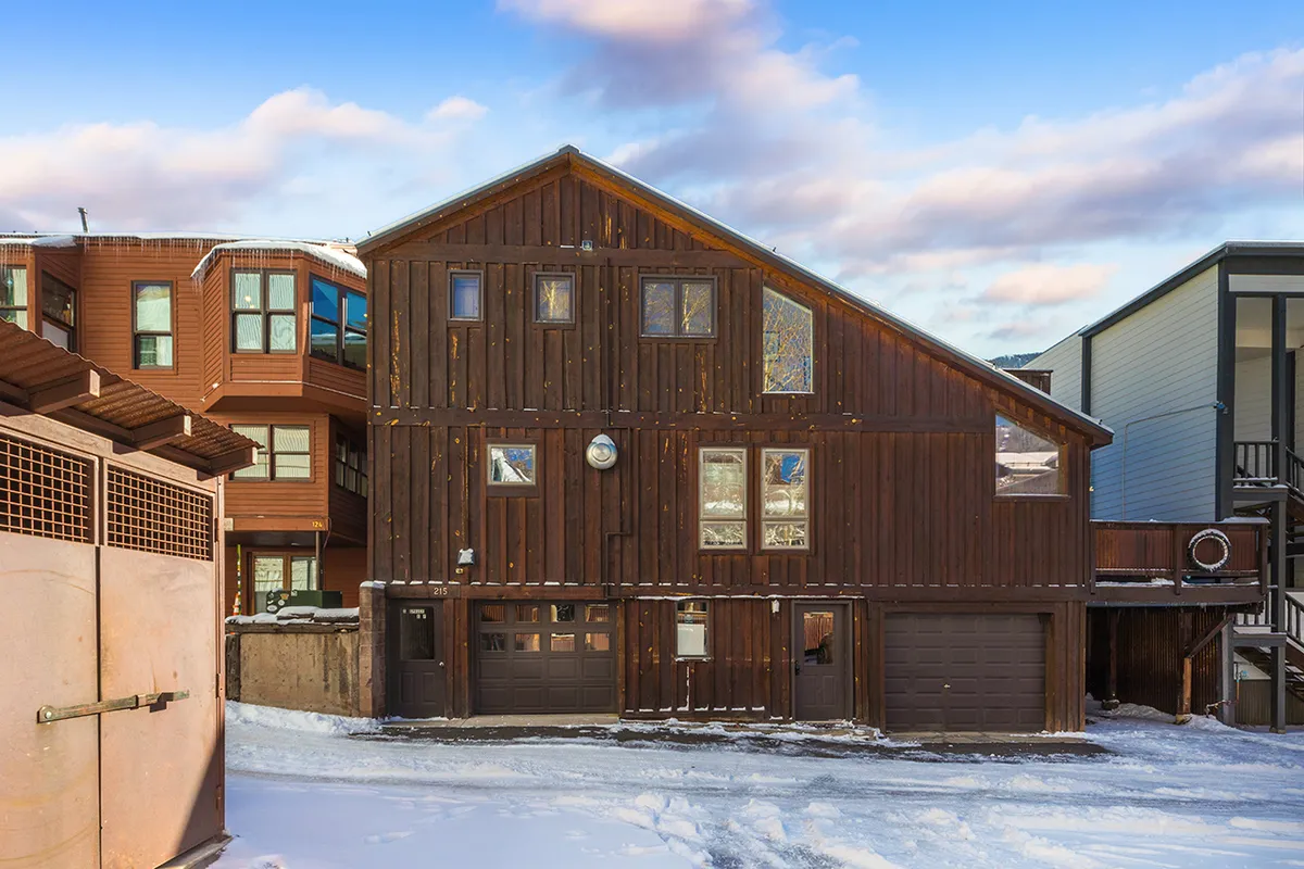 A welcoming exterior view of the property with a wooden facade, large windows, and garage doors, set against a backdrop of snow-covered ground. The fresh snow hints at winter activities nearby, while the expansive windows suggest a strong connection between indoor living and the vibrant Telluride outdoors.