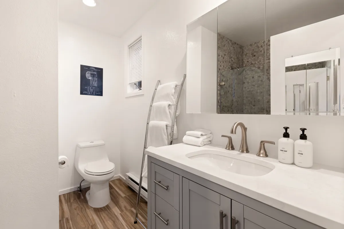 A modern, well-lit bathroom with a vanity featuring dual sinks, a large mirrored cabinet, a separate shower area, toilet, and an organized towel rack. The space looks serene and functional, designed for multiple people to prepare for their day efficiently.